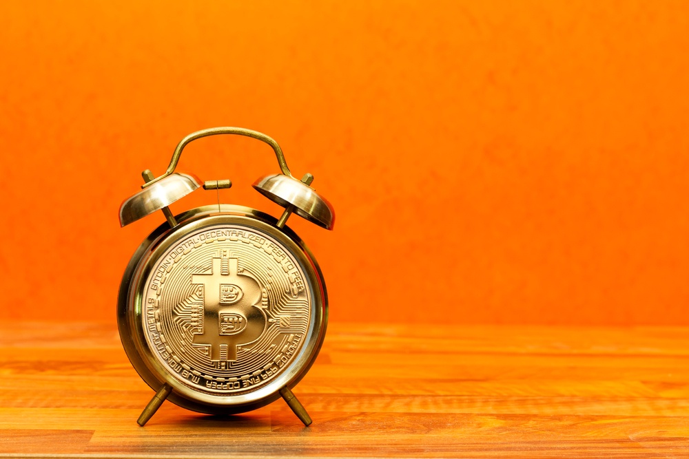 bright orange background with vintage alarm clock and bitcoin logo on face 