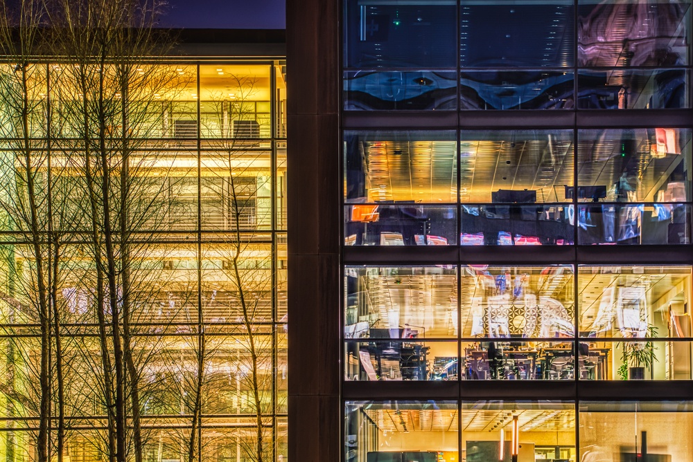 Contemporary office with a glazed facade at night in the financial district. Warm lights at night through the window and office chairs 