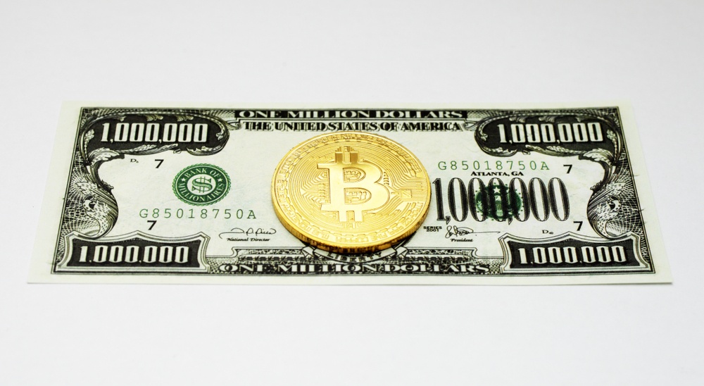 a million dollar note against a white background, with a bitcoin on top, signifying the idea that bitcoin might reach  alt=