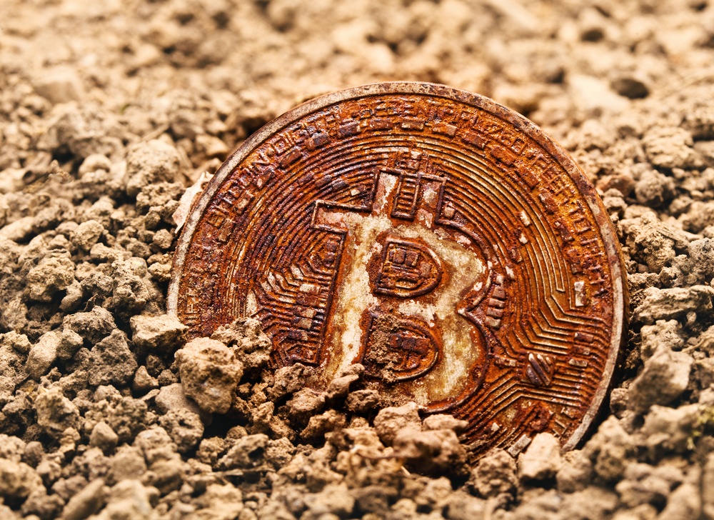 close photo of rusted bitcoin physical coin in dry yellow sand and dirt 