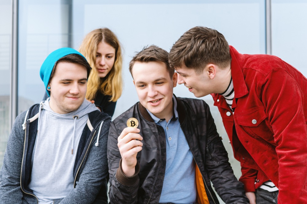 four friends talking about bitcoin and looking at a physical bitcoin 