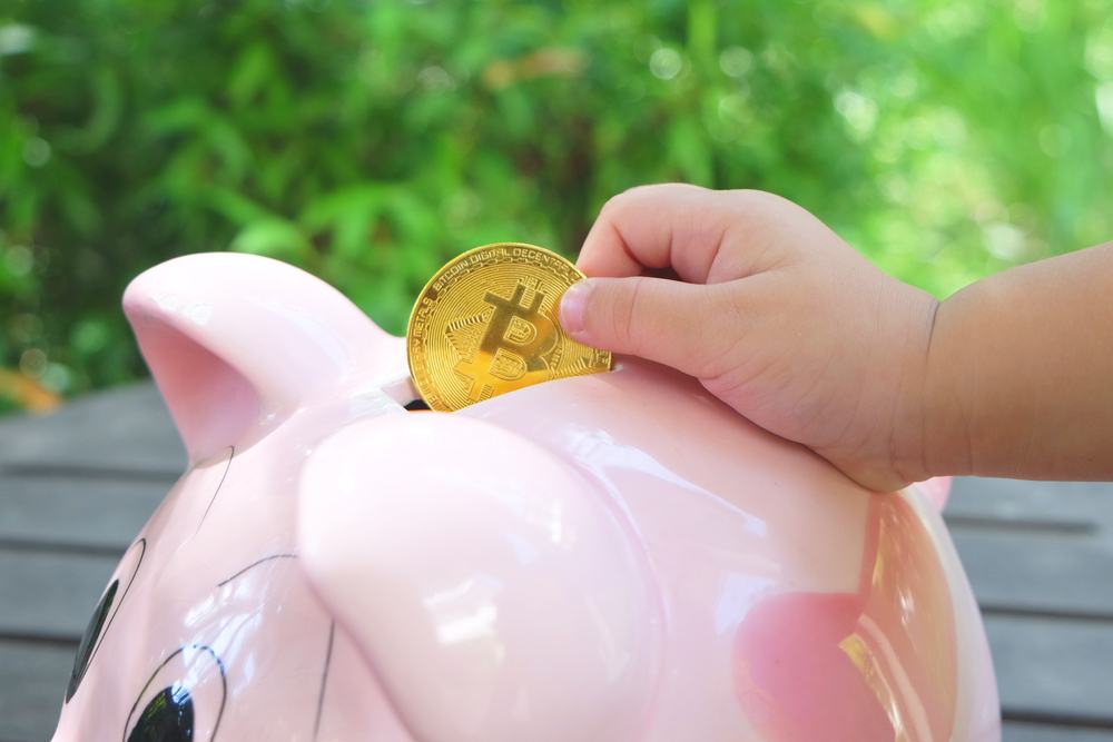 outdoor photo of large pink piggy bank and bitcoin deposit with child 's hand