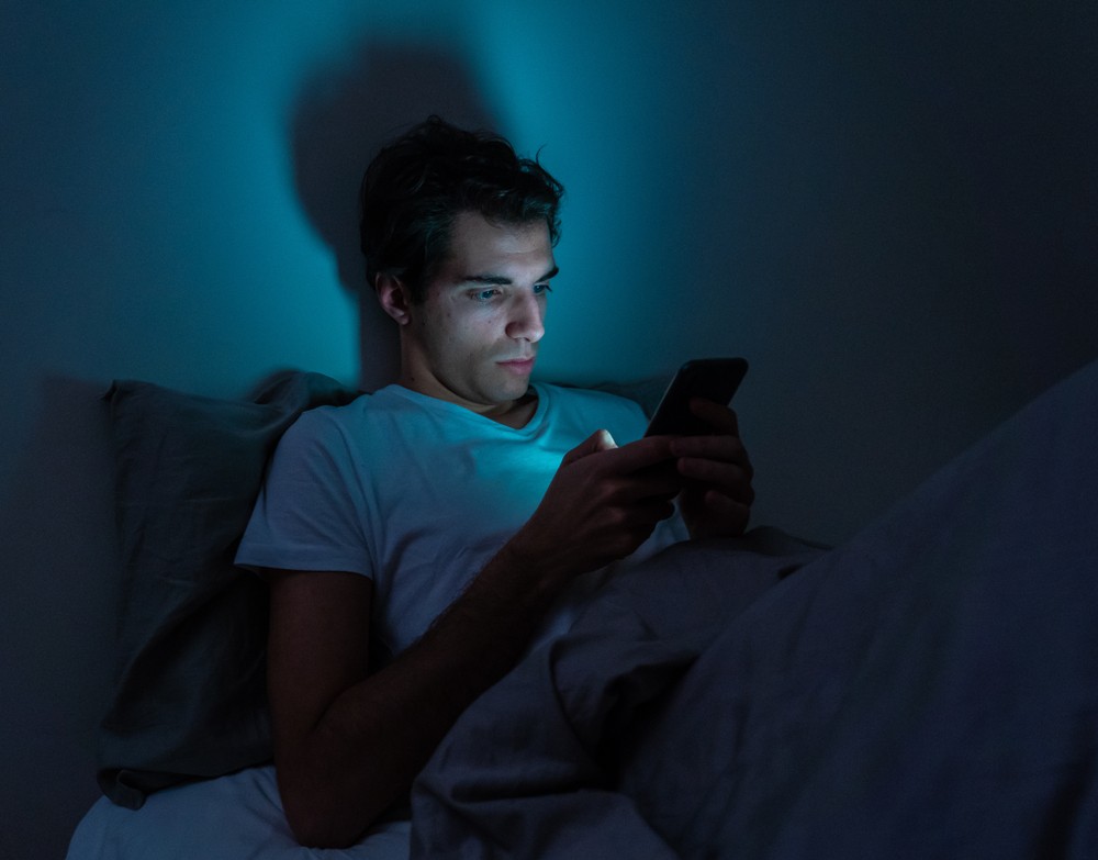 young man checking bitcoin price in the middle of the night in bed 