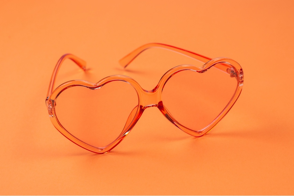 heart shaped glasses with orange frames and lenses on orange background 