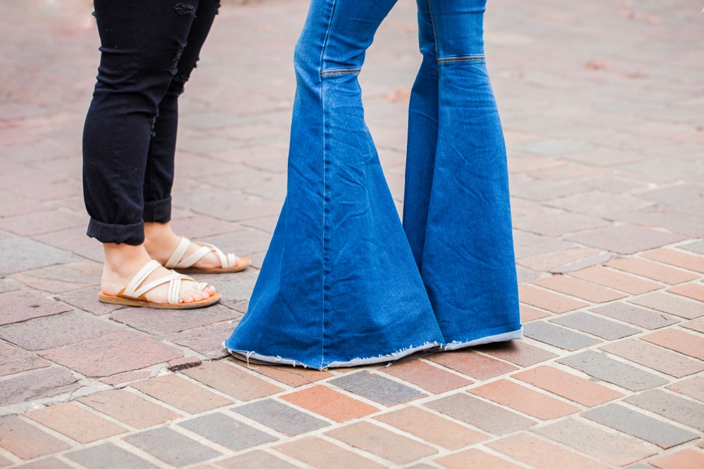 woman wearing large bell bottom denim jeans on stone pathway 