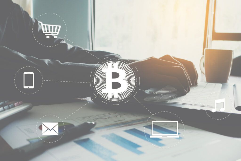 Man typing at the computer with bitcoin logo and lines drawn to icons representing digital life like commerce, communication, and business 