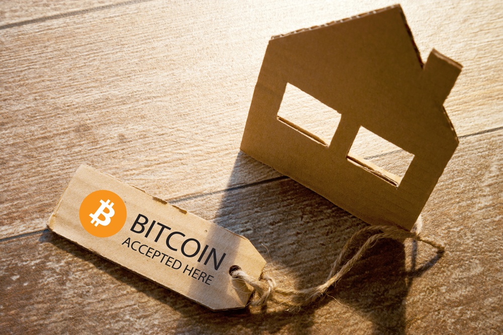 buy a house with bitcoin. house silhouette with low light on wood background with cardboard price tag with bitcoin logo 