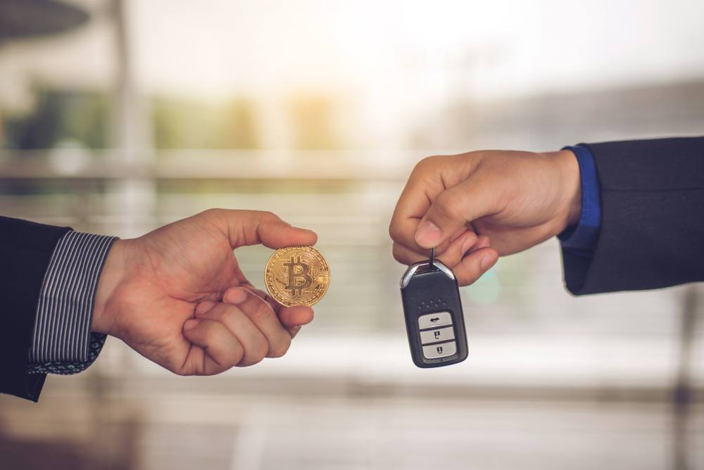 buy a car with bitcoin. two men exchanging physical bitcoin for car keys at a car dealership 