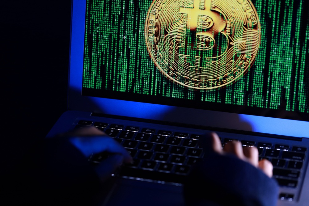 can bitcoin be hacked? A man using a laptop with matrix-like symbols running behind a bitcoin logo, suggesting that he is a hacker 