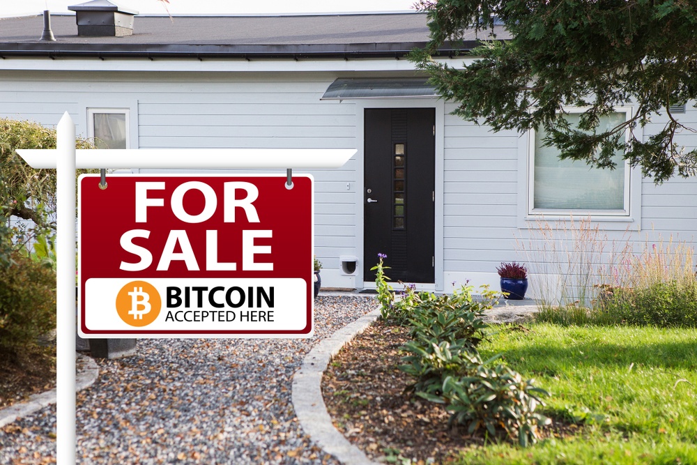 A real estate sign saying  "For Sale. Bitcoin Accepted Here", outside a white house with a black front door