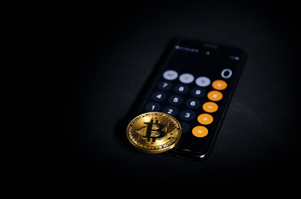 A calculator with a physical bitcoin on top of it, in a dark room. 