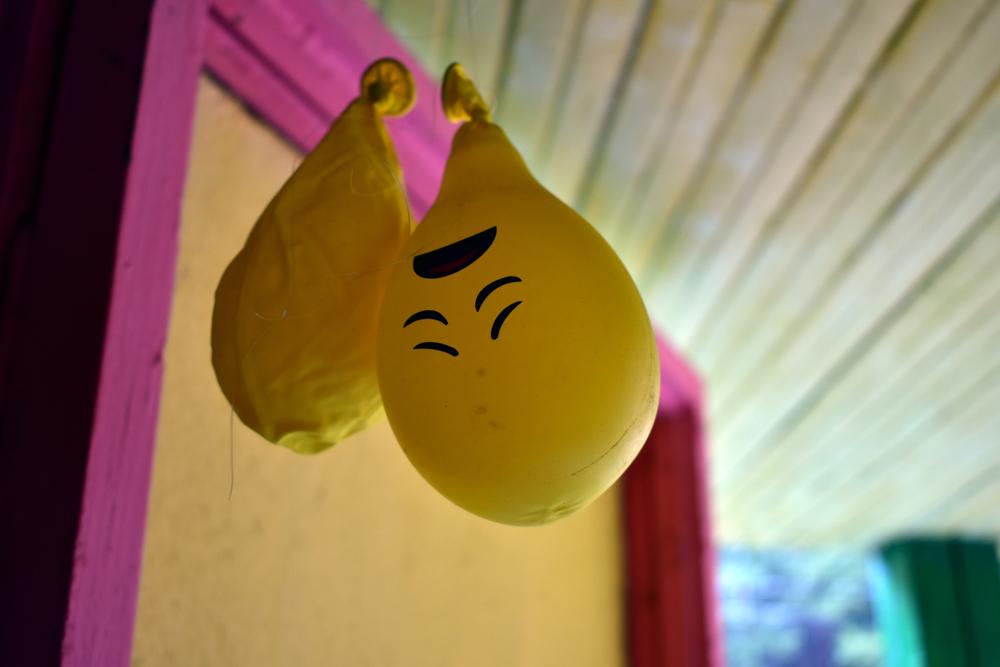 Two deflated ballons, one with a sad face, hanging upside down 