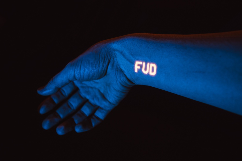 F.U.D. written in mechanical, reflective letters highlighted on wrist. dark ambient background 