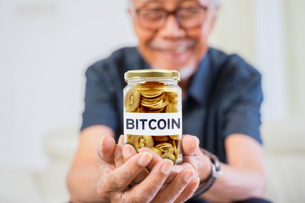 An out of focus old man holding a jar of physical bitcoins, with the label bitcoin on the jar 