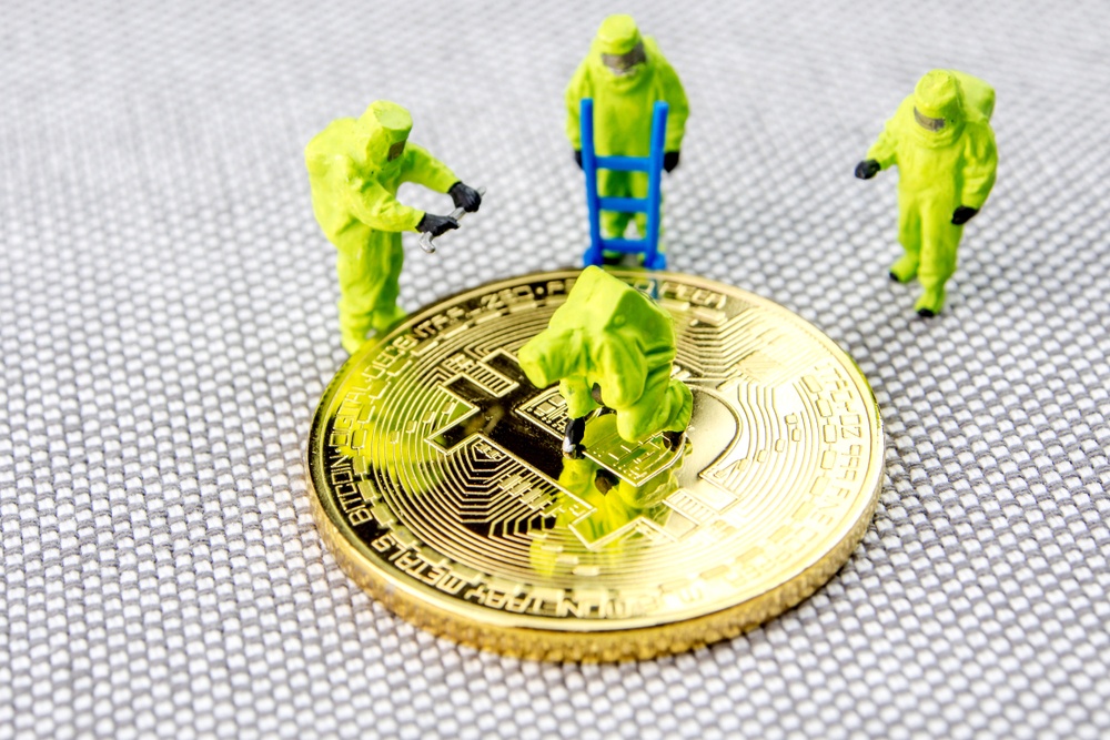 Toy men in radiation suits examining a single large physical bitcoin 