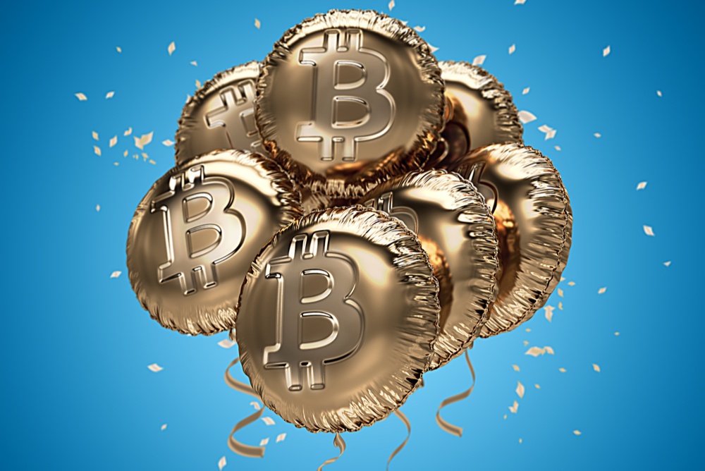 Golden balloons with the bitcoin symbol, against a blue background with confetti, highlighting the idea of a celebration 