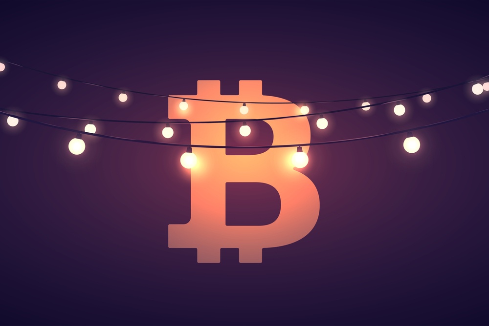 A bitcoin logo against a dark background, with strings of lights in front of it, showcasing the idea of celebrating bitcoin or bitcoin holidays 