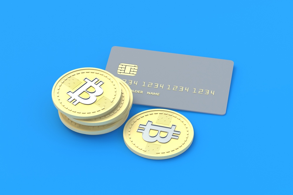 A graphic image of physical bitcoins in front of a credit card, in front of a light blue background 