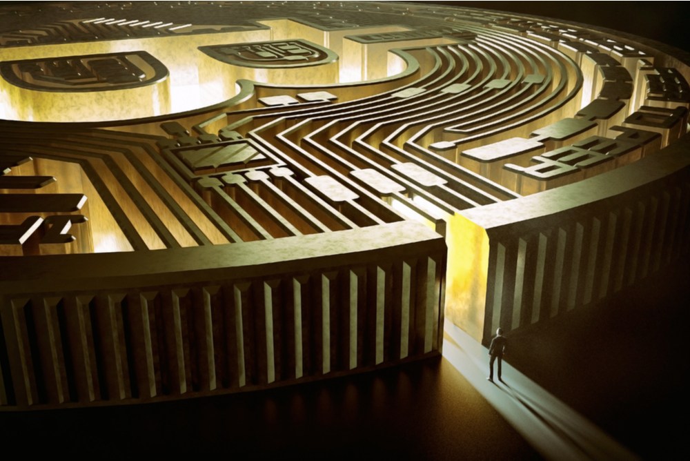 A representation of a giant bitcoin that has been made to look like a maze, with a man standing at the entrance 