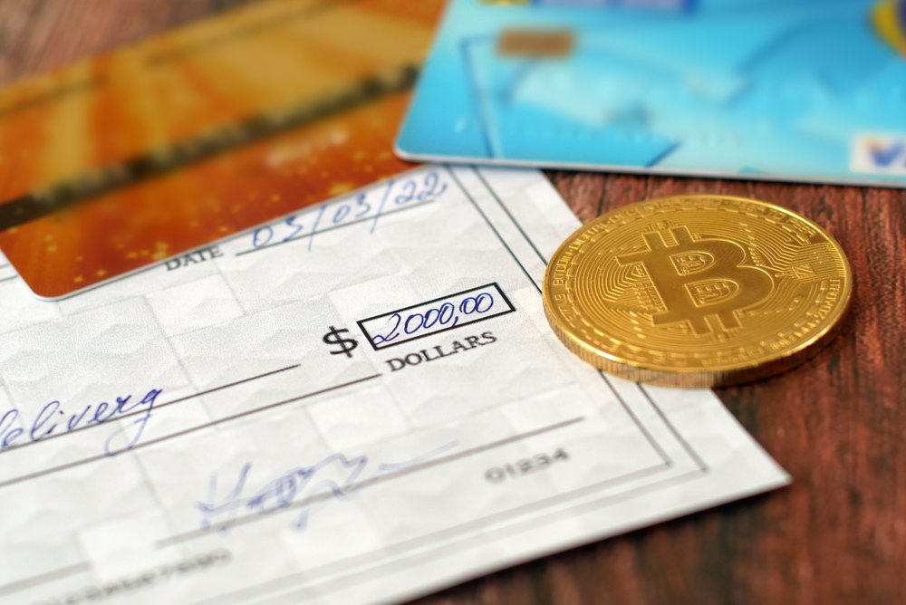 traditional bank check and bitcoins sitting on wooden table. getting a paycheck in bitcoin 