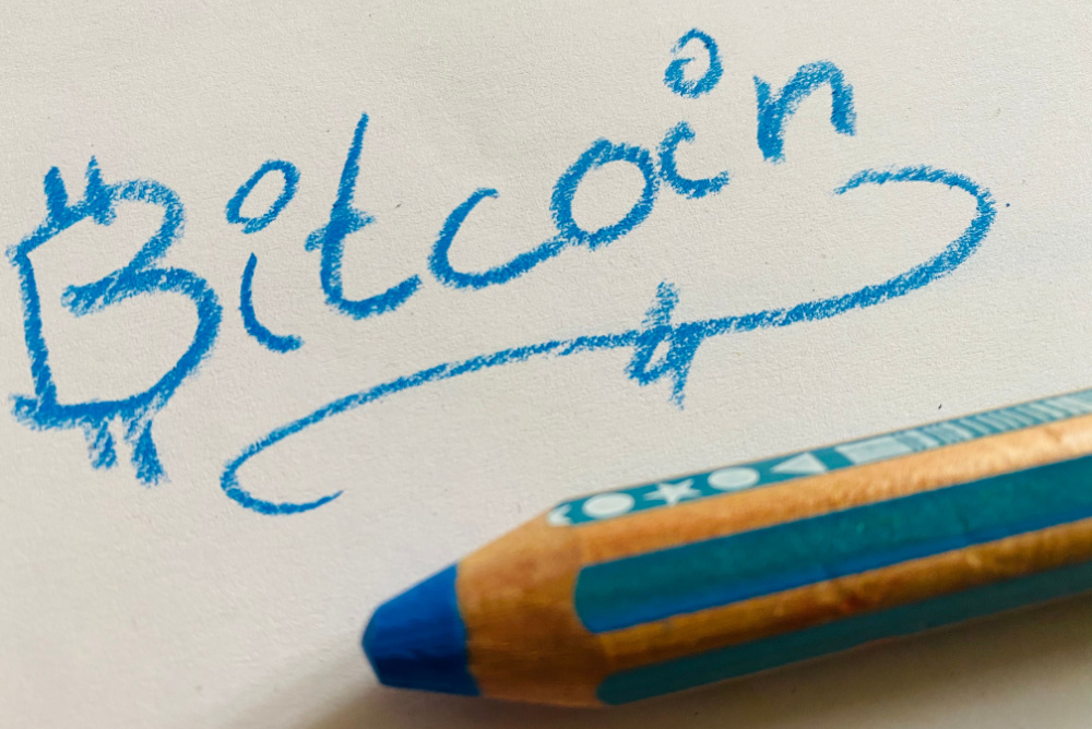 blue colored pencil writing out the word  "bitcoin" in childish handwriting